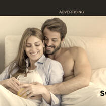 a couple sitting upright in bed. they are holding each other and smiling. above them is a dark grey banner with the word "advertising" in white text. this is cropped from tumblr's "sweaty in bed" ad